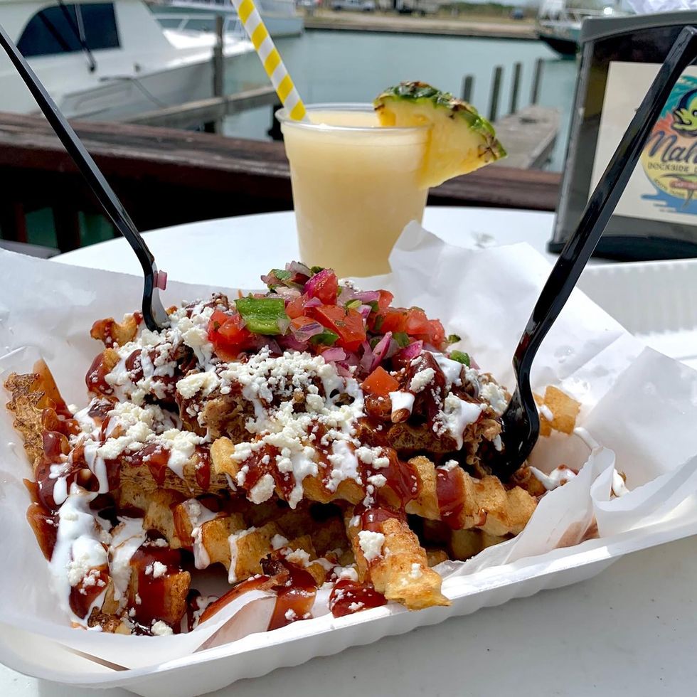 plate of loaded fries with a frozen pina colada beside the water at mahi nic on south padre island, texas