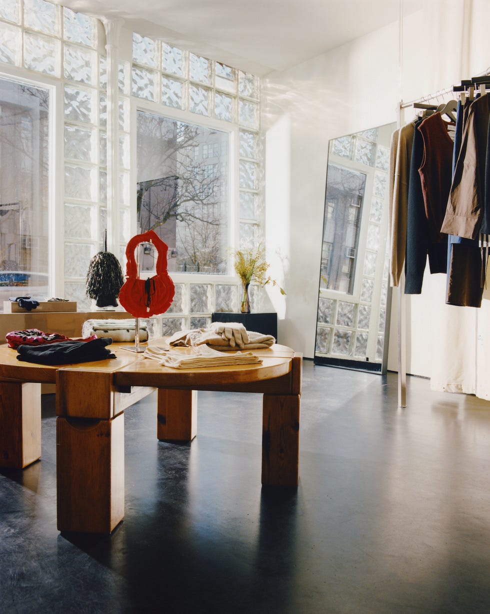 a round wooden table with merchandise on it sits inside the boutique maimoun, which has a glass brick facade