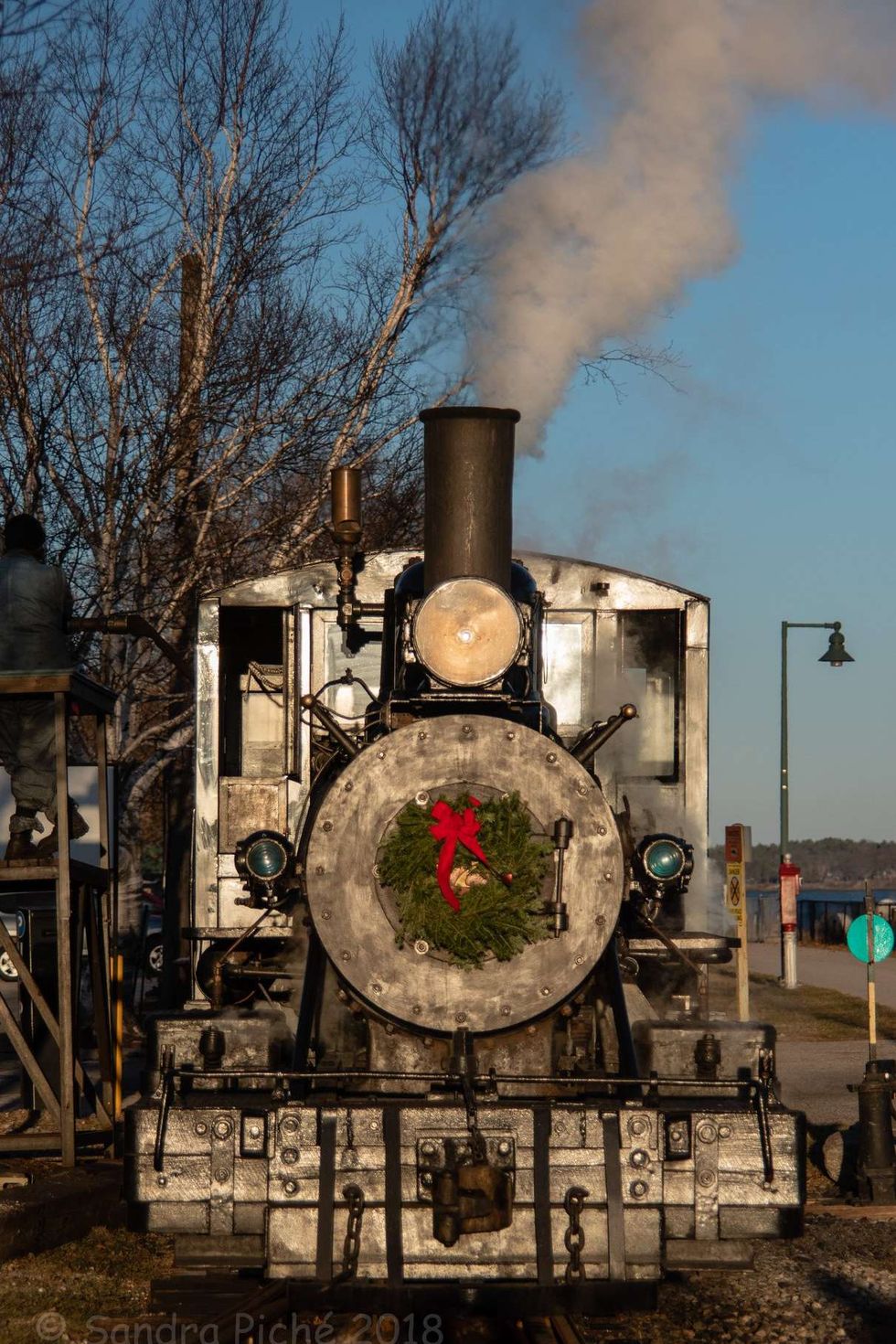 vintage locomotive with headlight on and stream coming out of pipe, with a christmas wreath with a big read bow affixed to the front