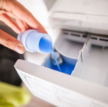 a hand pours fabric softener into a washing machine