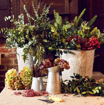 to brighten dark days, florist sarah williamson weaves rustic wreaths in her wiltshire farmhouse, inviting others to learn the skill at winter workshops pod pipbucket fulls of stems, berries and winter flowers , lit candles in background