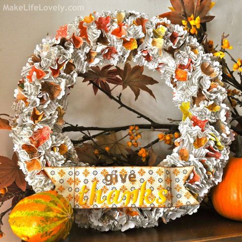 thanksgiving wreath made out of punched print paper with sign at the bottom that reads give thanks