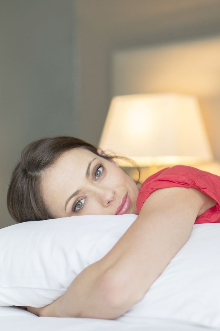 Portrait of beautiful woman wearing red dress lying on bed and hugging pillow