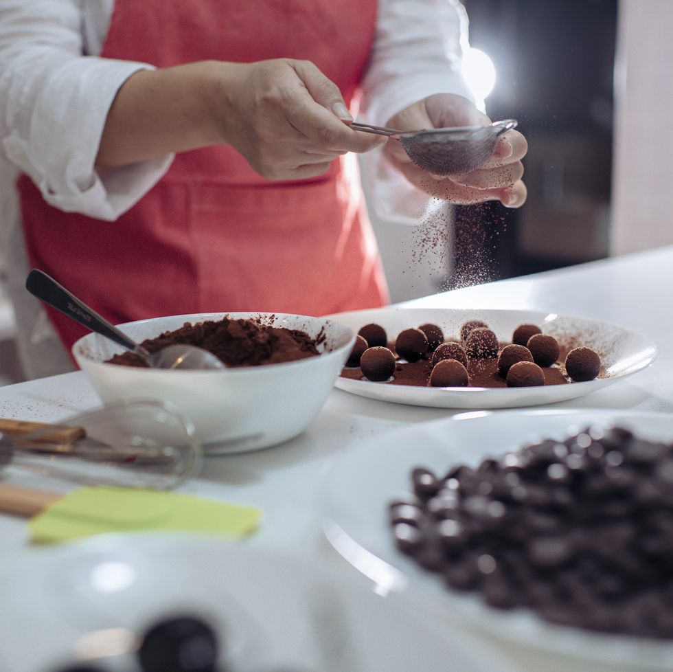 an asian chinese mid adult female dessert chef dusting and coating chocolate truffles in the domestic kitchen