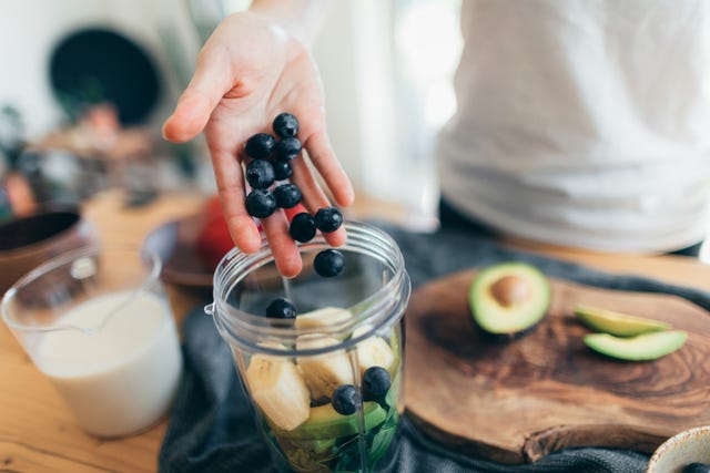 vrouw maakt een smoothie met blauwe bessen, avocado en banaan in een blender