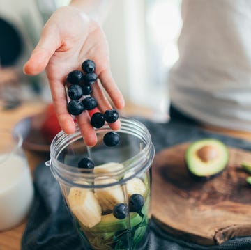 vrouw maakt een smoothie met blauwe bessen, avocado en banaan in een blender