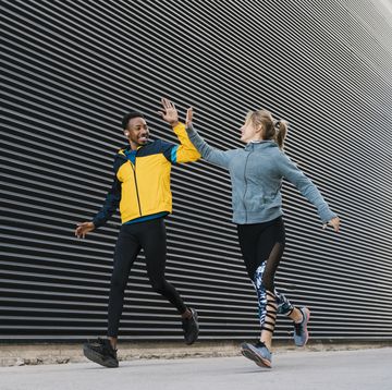 male and female sportsperson doing high
five while running on sidewalk during sports training by wall