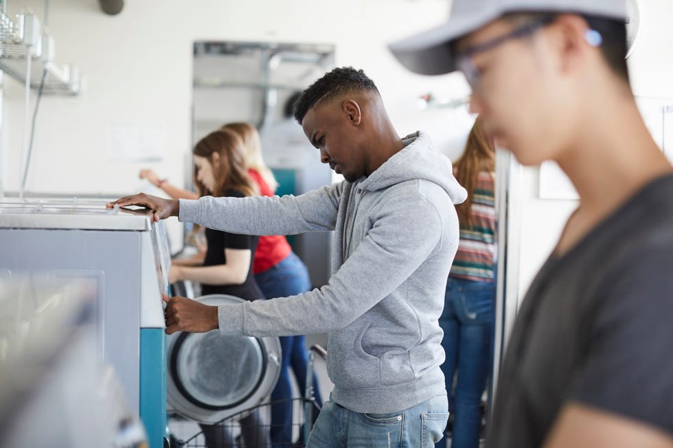male and female university students using washing machine at laundromat
