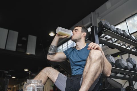 male athlete drinking protein shake while sitting in gym