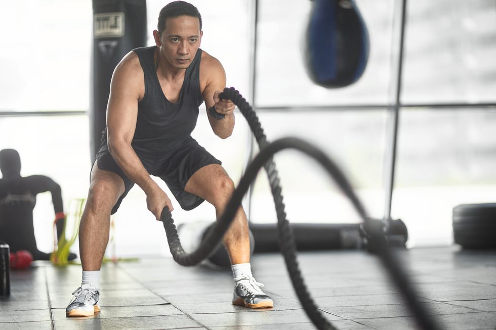 male athlete exercising with battling rope in gym
