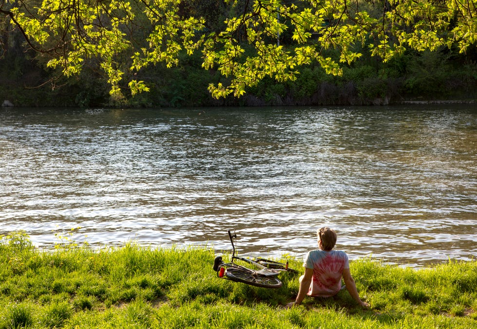 male bicyclist pauses at river edge, looks off