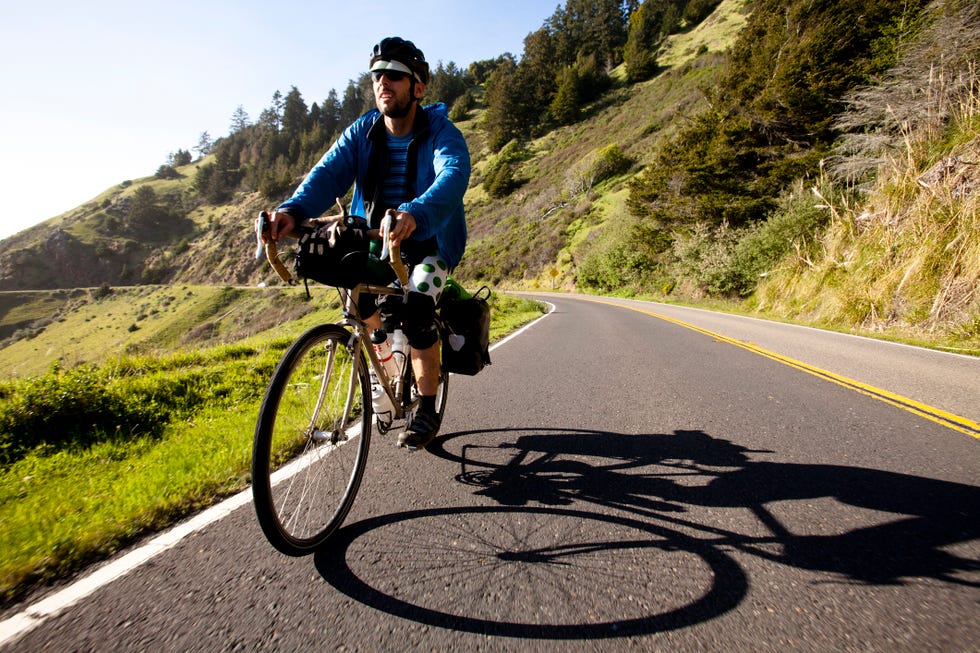 a male cyclist rides his touring bike down the pacific coast highway near jenner, california