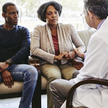 male doctor comforting mature woman sitting with son in hospital waiting room