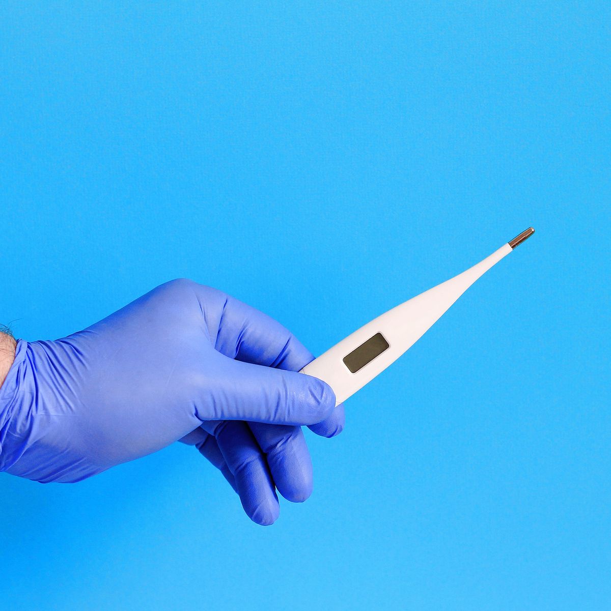 Male doctor holding digital thermometer on blue background, closeup.