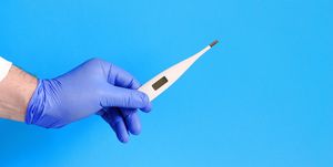 Male doctor holding digital thermometer on blue background, closeup.