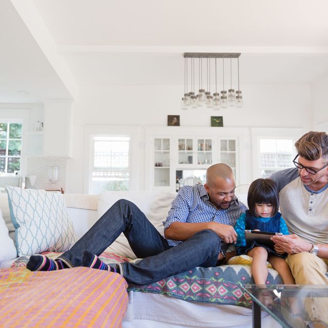 Male gay parents and adopted toddler daughter using digital tablet on living room sofa