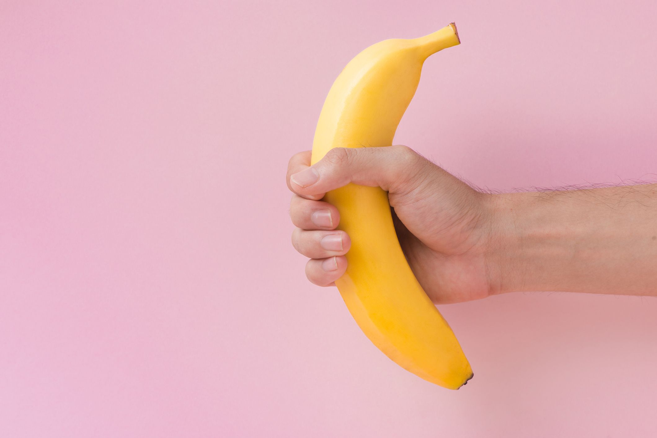 male hand holding a banana isolated on pink background