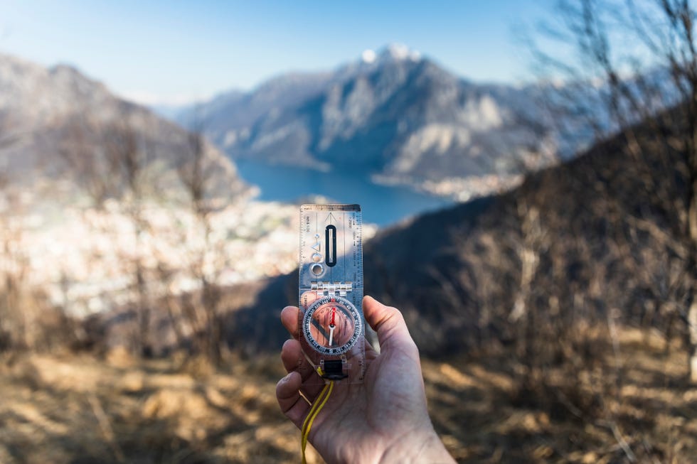 male hand with compass, mountains range in background, sunny day
