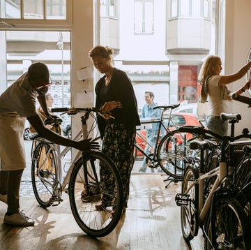 male owner repairing bicycle of senior customer while colleague working on bike at workshop