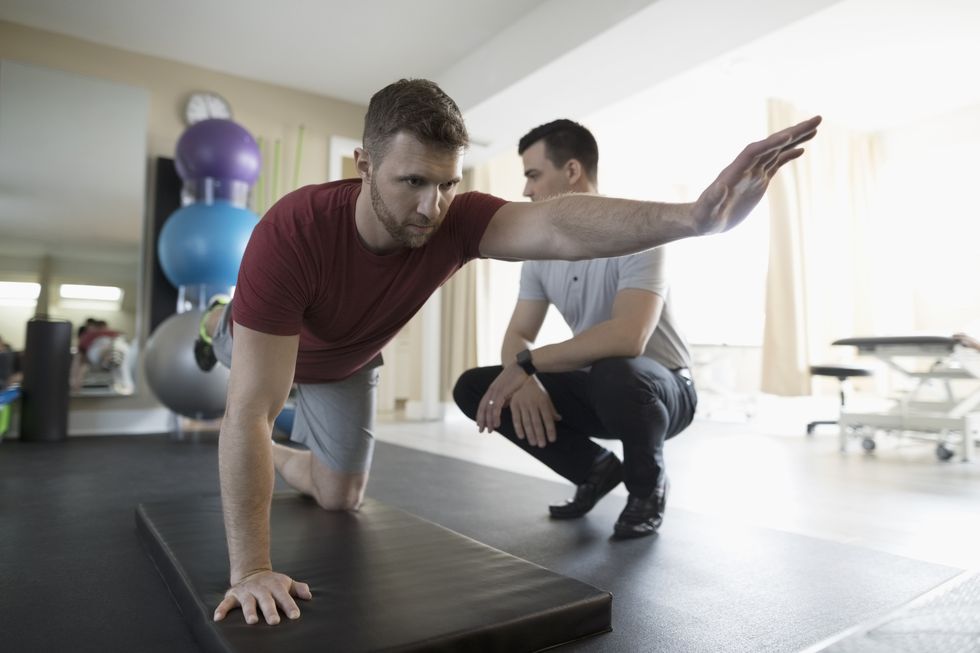 Male physiotherapist guiding client balancing in clinic gym