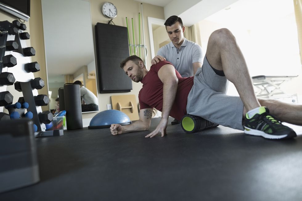 Male physiotherapist guiding client stretching in clinic gym