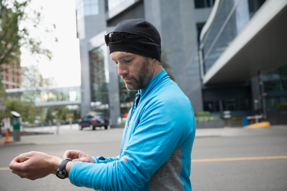 Male runner adjust smart watch band on urban street