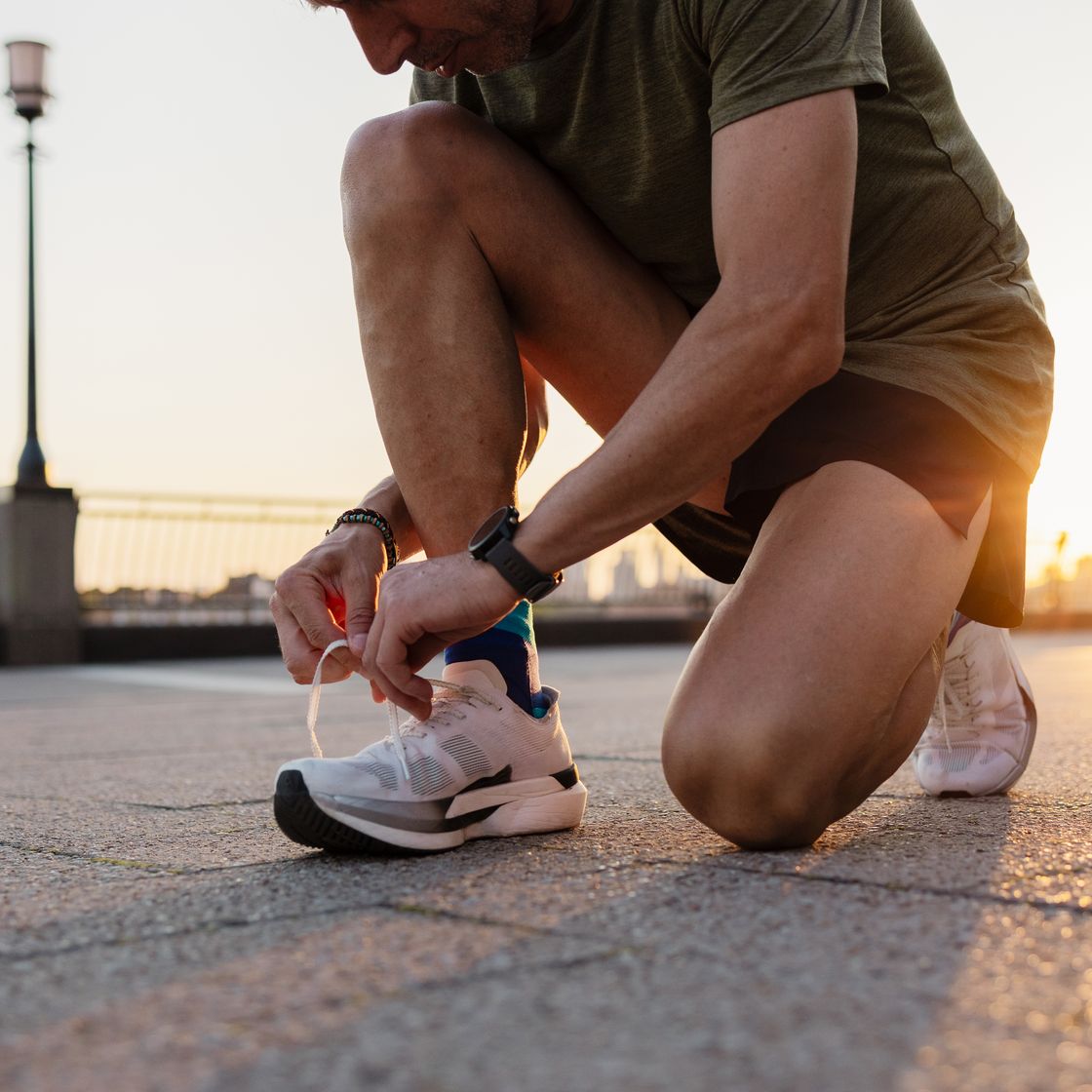 male runner tying shoelaces on running shoes before workout at sunset