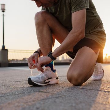 male runner tying shoelaces on running shoes before workout at sunset