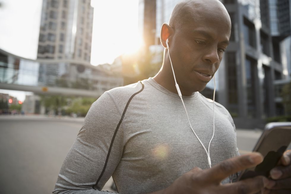 Male runner using smart phone, listening to music with earbud headphones on urban street