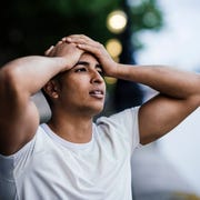 Male runner with hands on forehead taking a break on riverside running headaches