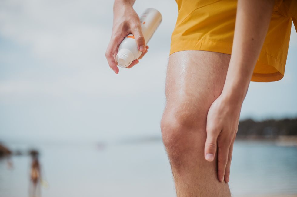a male spritzes his leg with spray sun screen at beach