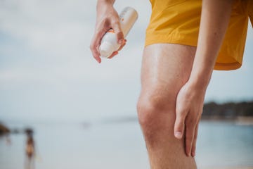 a male spritzes his leg with spray sun screen at beach