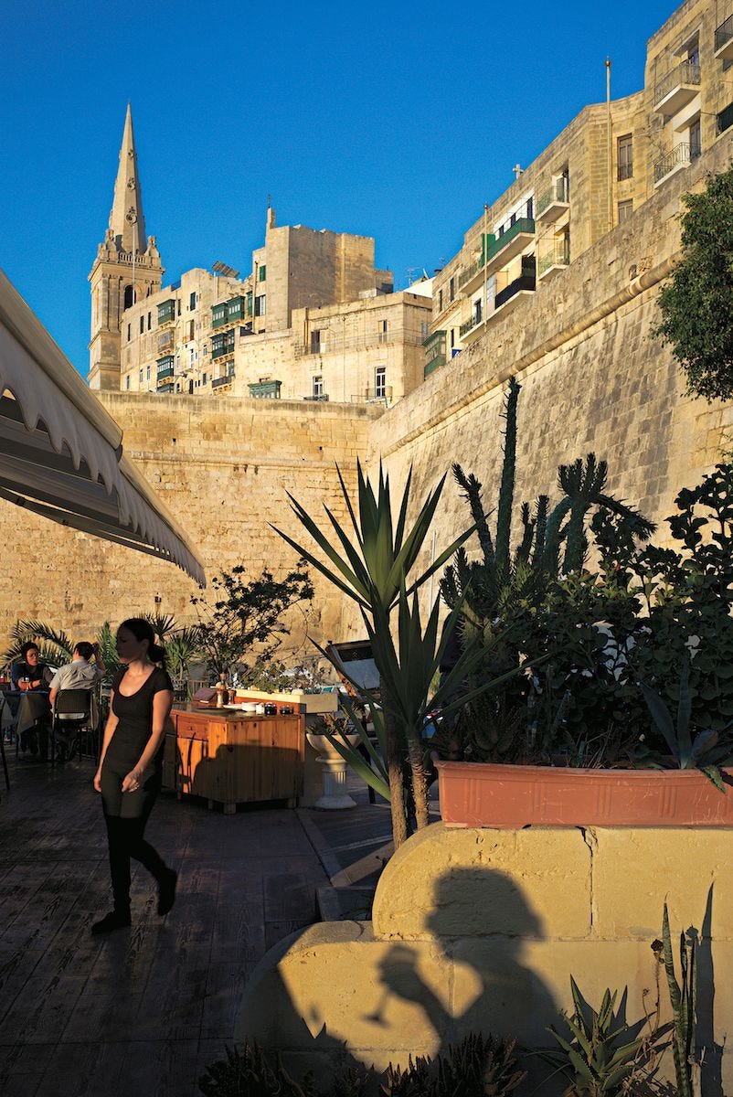 De zonsondergang werpt speelse schaduwen bij Cockneys een restaurant in het historische centrum van Valetta