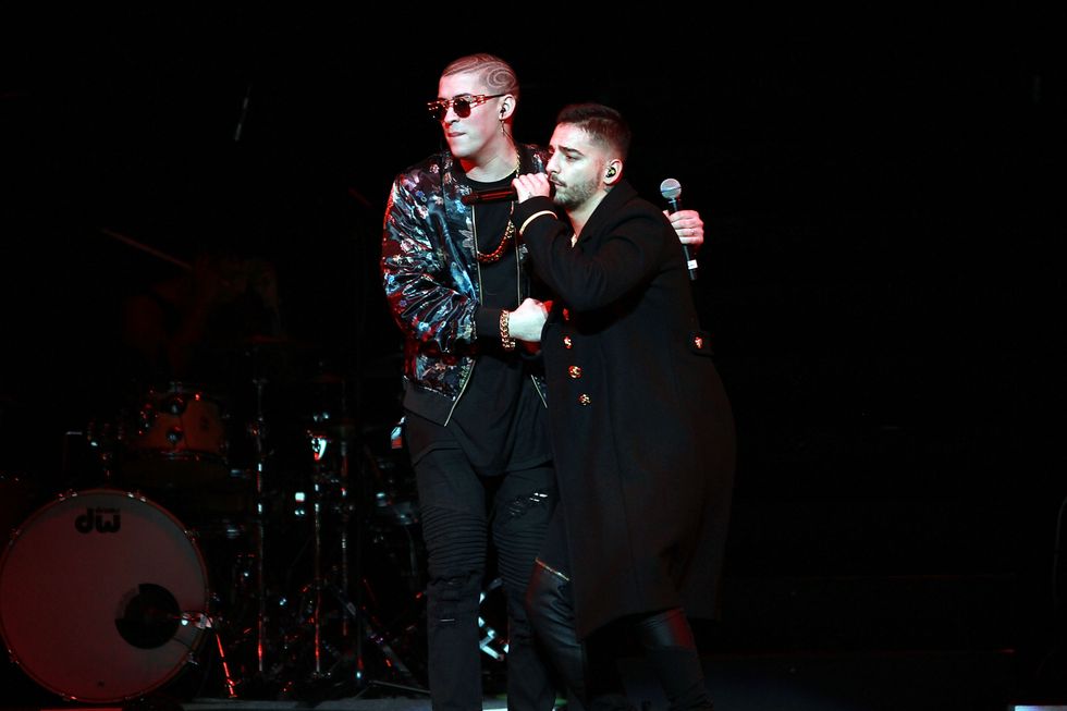 maluma and bad bunny embracing each other on a stage as bad bunny sings into a microphone and maluma looks out at the crowd