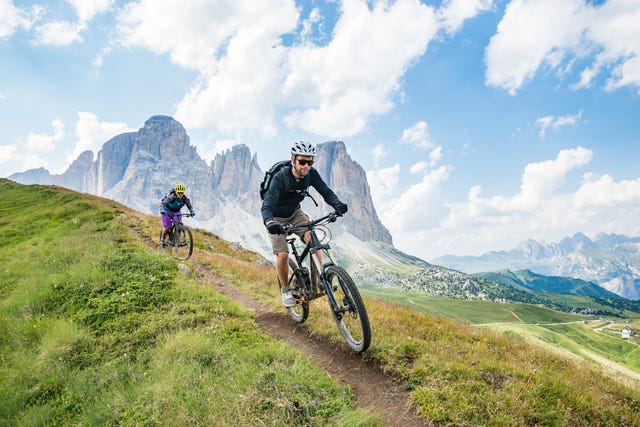a man and a woman on mountain bikes racing along trail in the dolomites, val gardena, italy