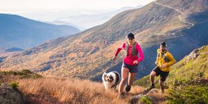 man and woman trail running with dog in mountains at sunrise