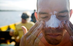 Man applies white zinc to his face and nose while sitting on a boat.