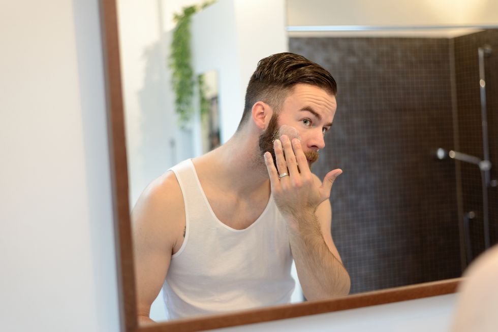 man applying beauty product reflecting on mirror