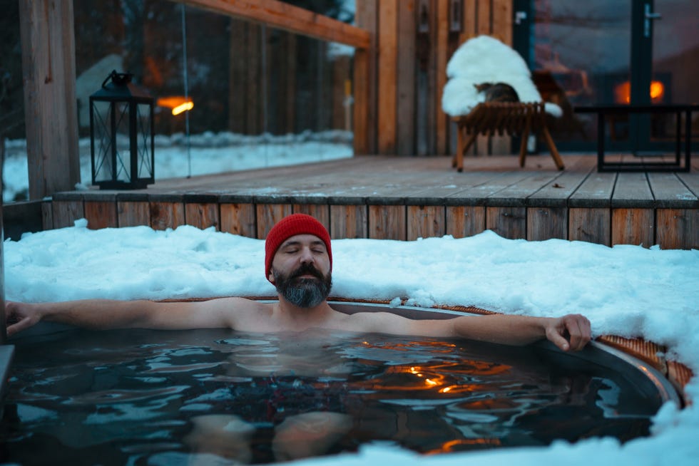 man bathing in wood burning hot tub, enjoying hot water during cold, snowy winter evening unique bathing experience during relaxing winter weekend in cabin in mountains concept of hygge winter, peaceful, cozy moments for yourself