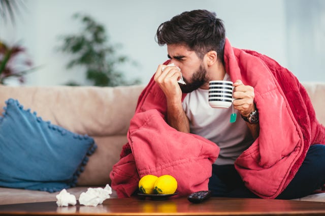 man blowing his nose while lying sick in bed