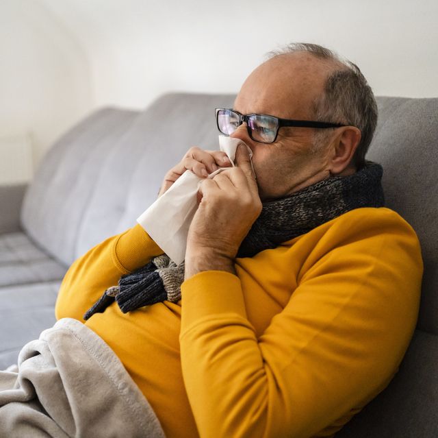 man blowing nose sitting on sofa at home