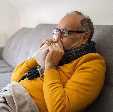 man blowing nose sitting on sofa at home