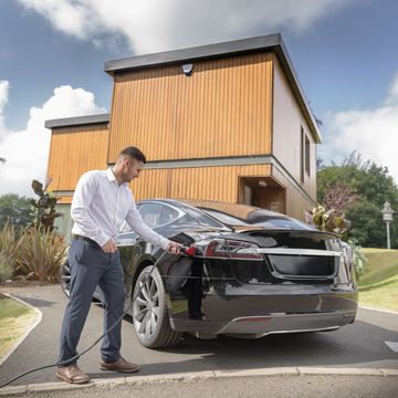 man charging electric car outside modern house