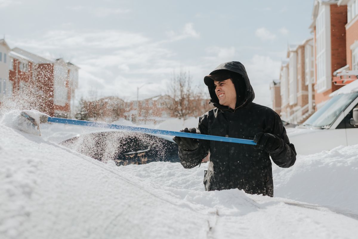man clearing snow covered vehicle with broom, toronto, canada