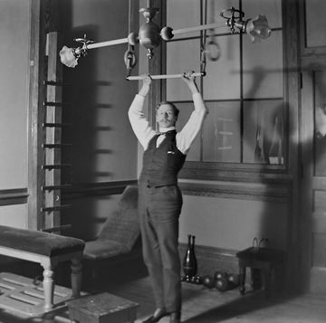 a man demostrates some exercise equipment in a gym, ca 1895