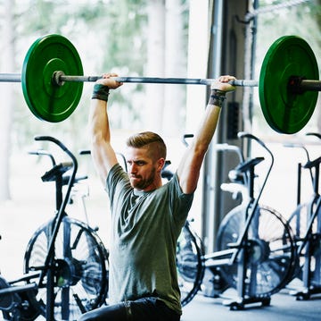 man doing lunges with barbell overhead in gym