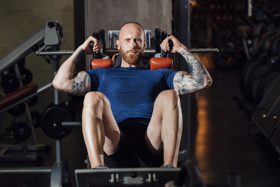 man doing quadriceps exercise on hack squat machine at gym