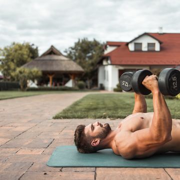 dedicated shirtless muscular caucasian man doing exercises with dumbbel outdoor fitness concept