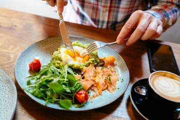 man eating avocado toast with egg, salmon and arugula salad for brunch at the restaurant