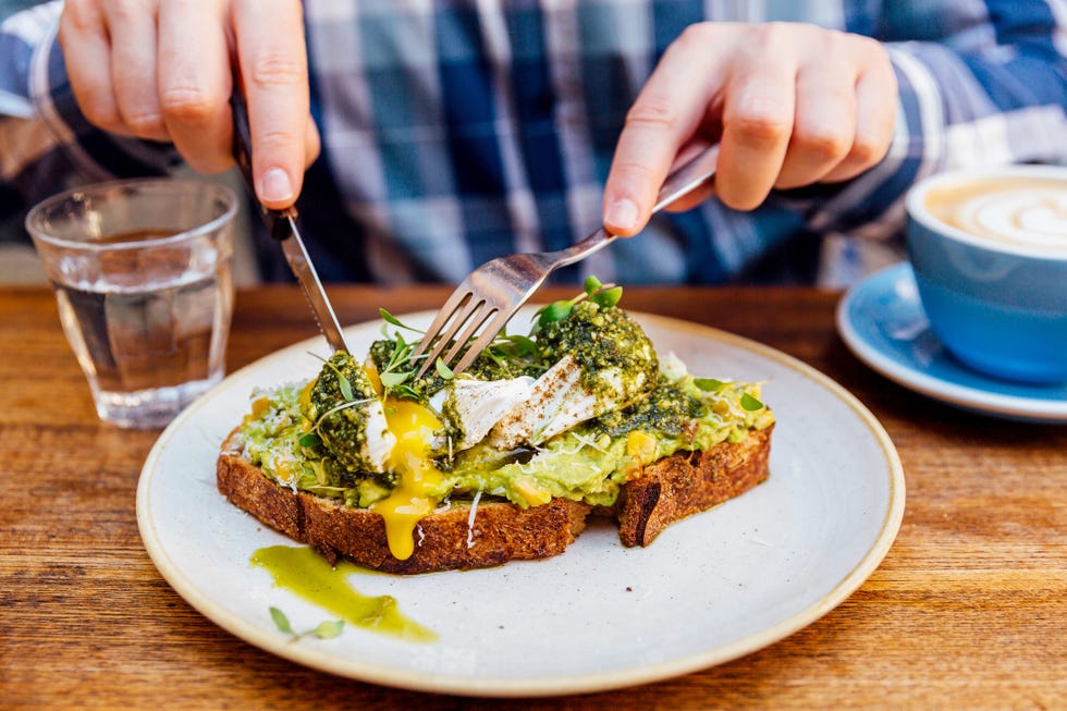 man eating avocado toast with poached egg, close up